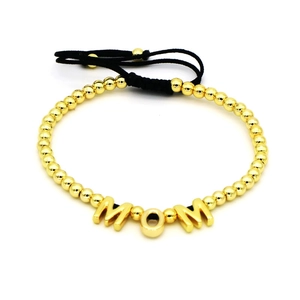Detail of adjustable black cord bracelet featuring gold MOM letters and round beads