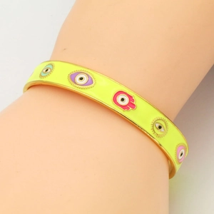 Detail of neon yellow enamel cuff bracelet featuring colorful evil eye and Hamsa hand motifs