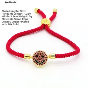 Detailed view of red braided bracelet with pink zircon smiley face charm and 18K gold plating