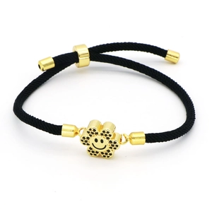 Macro detail of adjustable black woven rope bracelet with gold smiling flower charm