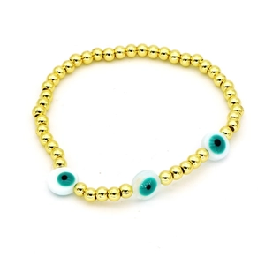 Dettaglio del bracciale con perline dorate e ciondoli a forma di occhio turco su bianco