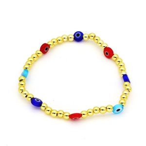 Dettaglio del bracciale con perline dorate e ciondoli colorati Evil Eye su sfondo bianco puro