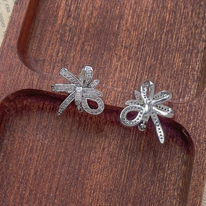 Detail of silver bow earrings featuring micro-pave cubic zirconia on dark wood