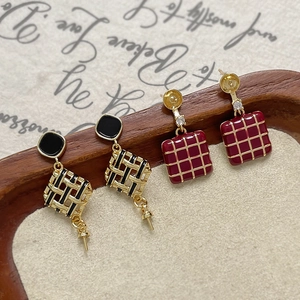 Dettaglio orecchini geometrici con pendenti a trama nera e a quadri rossi stile vintage