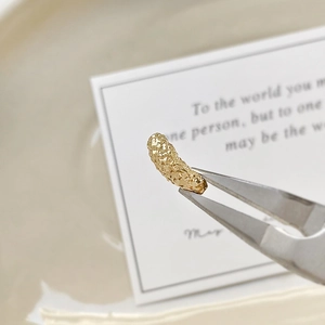 Macro shot of 18k gold-plated irregular caterpillar tube bead held by silver tweezers