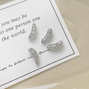 Close-up of four silver textured tube beads for DIY jewelry making on white card