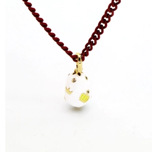 Detail of white enamel egg pendant with gold crown motif on a red rope necklace chain