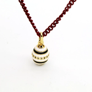 Macro detail of egg-shaped enamel pendant necklace with intricate gold trims and red cord