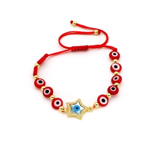Detail of red braided rope bracelet with zircon star charm and evil eye beads