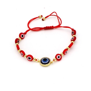 Detail of red braided Evil Eye bracelet with blue pendant and gold metal accents