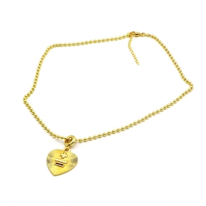 Détail d'un pendentif cœur doré avec rainures radiales et chaîne à boules sur fond blanc