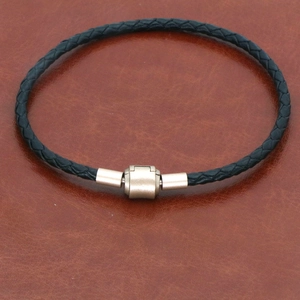 Gros plan du bracelet en cuir tressé noir avec fermoir magnétique doré mat sur cuir brun