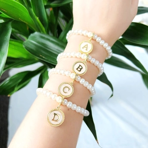 Close-up of pearl bracelets featuring gold-rimmed letter charms A, B, C, and D on wrist