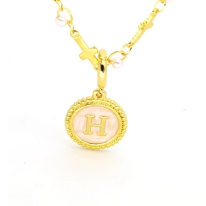 Vue macro du pendentif lettre H dorée avec émail rose, perles et breloque croix