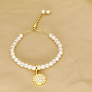 Detail of pearl bracelet with golden letter E pendant and adjustable sliding cord closure
