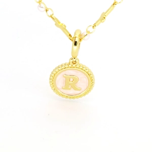 Détail macro du collier plaqué or avec pendentif lettre R en émail rose et perles blanches