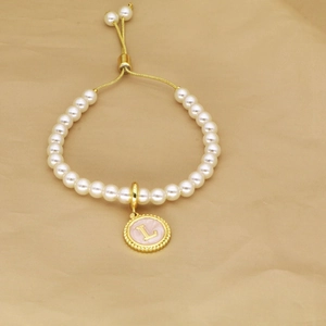 Detail view of gold adjustable clasp and white pearls with round letter L pendant