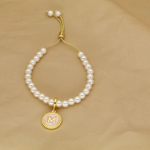 Detail of adjustable pearl bracelet with golden letter M pendant on beige fabric
