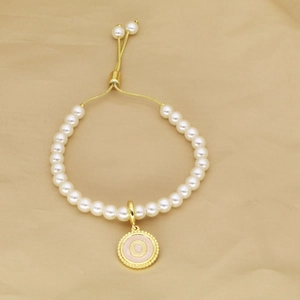Detail of pearl bracelet featuring a pink enamel letter O pendant and gold adjustable clasp