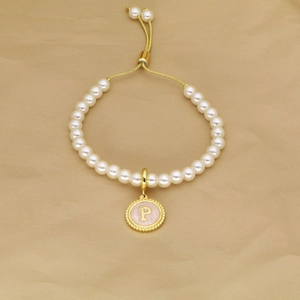 Detail of white pearl bracelet featuring a pink enamel letter P charm and golden toggle clasp