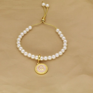 Detailed macro shot of white pearl bracelet with gold letter Q pendant and adjustable cord
