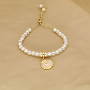 Detailed macro of a pearl bracelet featuring a gold letter R pendant and adjustable clasp