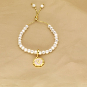 Detail of adjustable pearl bracelet with golden letter V charm on soft fabric