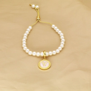 Detail of adjustable pearl bracelet with golden letter Y charm on textured paper