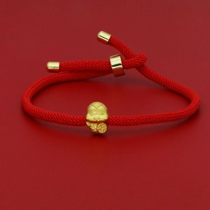 Macro detail of red woven bracelet with gold charm featuring a fortune character engraving