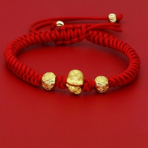 Macro view of hand-woven red cord bracelet with golden zodiac snake charm and lucky beads