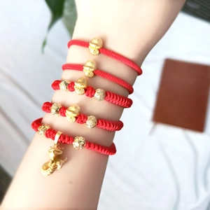 Detail of red braided bracelets with golden zodiac snake and wealth charms on wrist