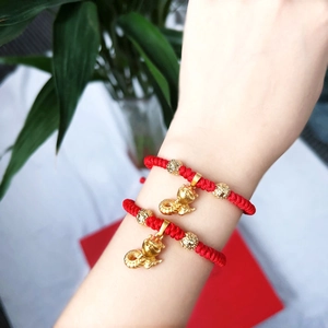 Detail of red braided zodiac bracelets with gold charms worn on a wrist for luck