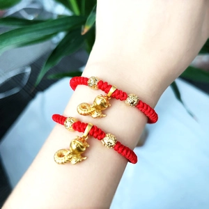 Detail of red braided zodiac snake bracelet with golden charms on woman's wrist