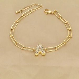 Macro detail of gold paperclip chain bracelet featuring a zircon-encrusted letter A pendant