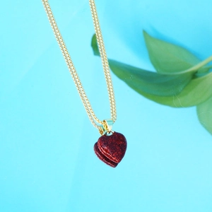 Détail macro d'un pendentif coeur rouge pailleté sur une chaîne de boîte dorée