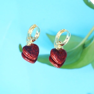 Détail de créoles dorées avec pendentifs cœur à paillettes rouges sur surface réfléchissante