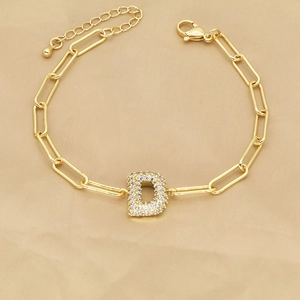 Macro detail of 18k gold paperclip chain bracelet with a sparkling zircon letter D charm