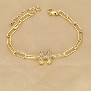 Close-up of 18k gold paperclip chain bracelet with a pavé zircon letter H pendant