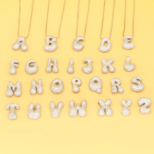 Puffy balloon style alphabet pendants with cubic zirconia inlay on a yellow background