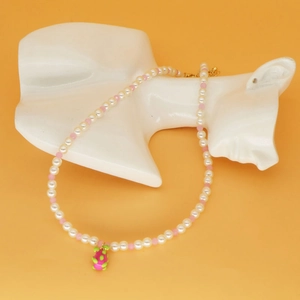 Gros plan du collier de perles avec pendentif fraise rose sur un mannequin de cou blanc