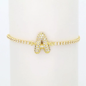 Close-up of golden tennis bracelet with pavé zircon bubble letter A on white stand