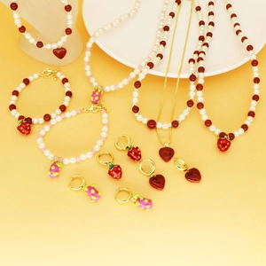 Détail de bijoux perlés avec pendentifs fraises rouges et cœurs posés sur un plateau