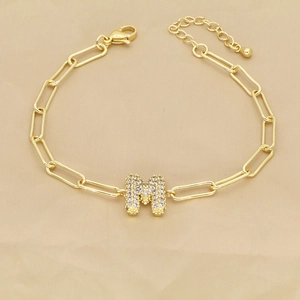 Macro detail of paperclip chain bracelet with a gold M letter pendant inlaid with zircons