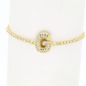 Detailed close-up of 18k gold tennis bracelet featuring a micro-paved zircon letter G