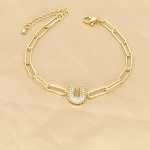 Detailed view of golden paperclip bracelet with a sparkling zircon letter U pendant