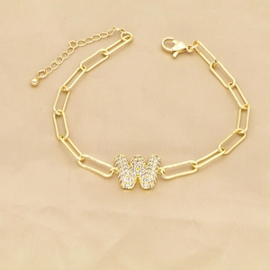 Macro detail of gold paperclip chain bracelet with zircon pavé letter W pendant