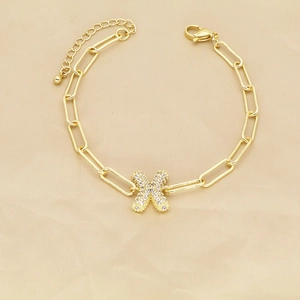 Detailed view of gold paperclip chain bracelet with a zircon-encrusted letter X pendant