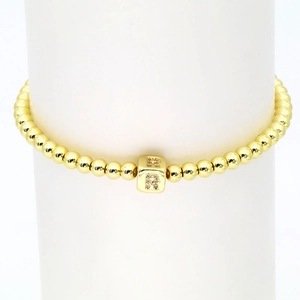 Detail eines 18k Goldperlenarmbands mit mikrobesetztem Zirkonia-Würfel und Buchstabe R