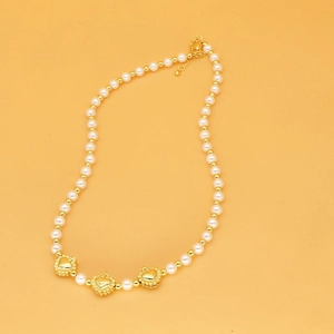 Détail du collier de perles avec trois pendentifs en cœur doré sur fond orange vif