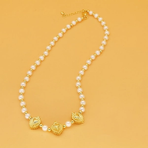 Détail du collier de perles blanches et dorées avec trois pendentifs en forme de cœur